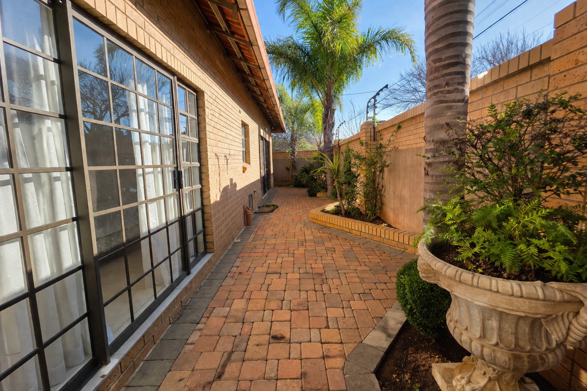 A well-maintained rear exterior walkway featuring brick paving, a raised planter bed, and large sliding glass doors providing access to the townhouse interior.