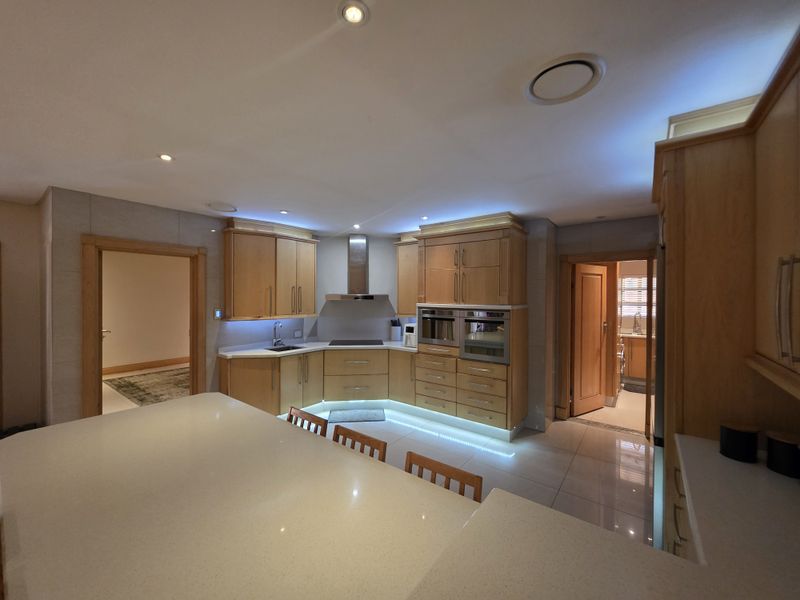 Modern kitchen featuring light wood cabinetry, stone countertops, integrated appliances, and a central island with recessed lighting and tiled flooring.