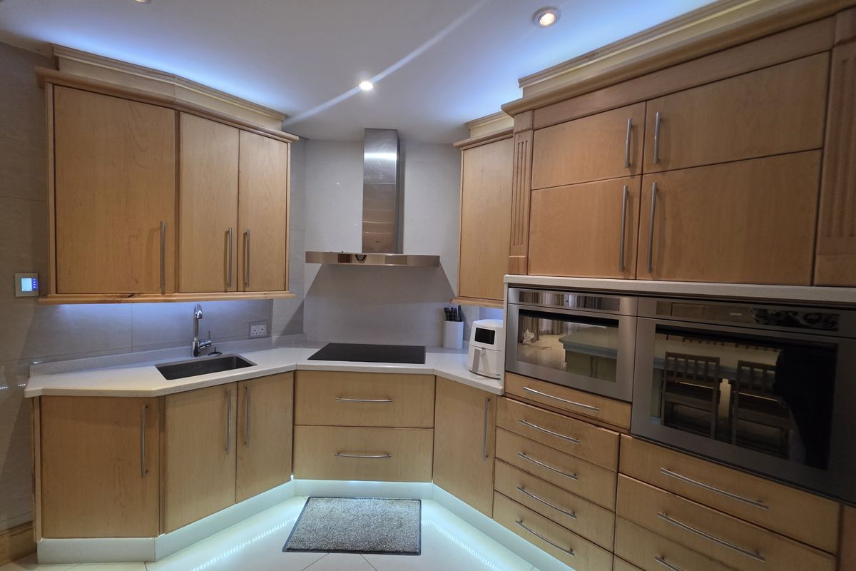 A well-appointed kitchen featuring warm wooden cabinetry, stone countertops, integrated stainless steel appliances, and modern LED accent lighting.