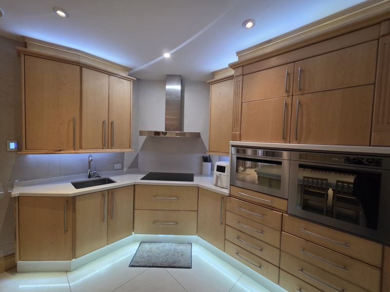 A well-appointed kitchen featuring warm wooden cabinetry, stone countertops, integrated stainless steel appliances, and modern LED accent lighting.