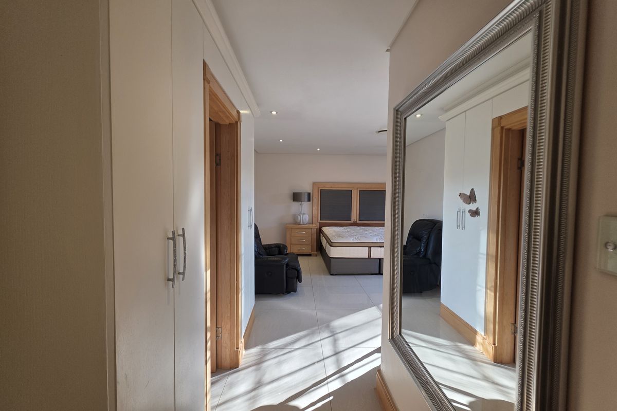 A spacious bedroom featuring built-in cupboards, tiled flooring, and recessed downlights, viewed from an adjacent hallway.