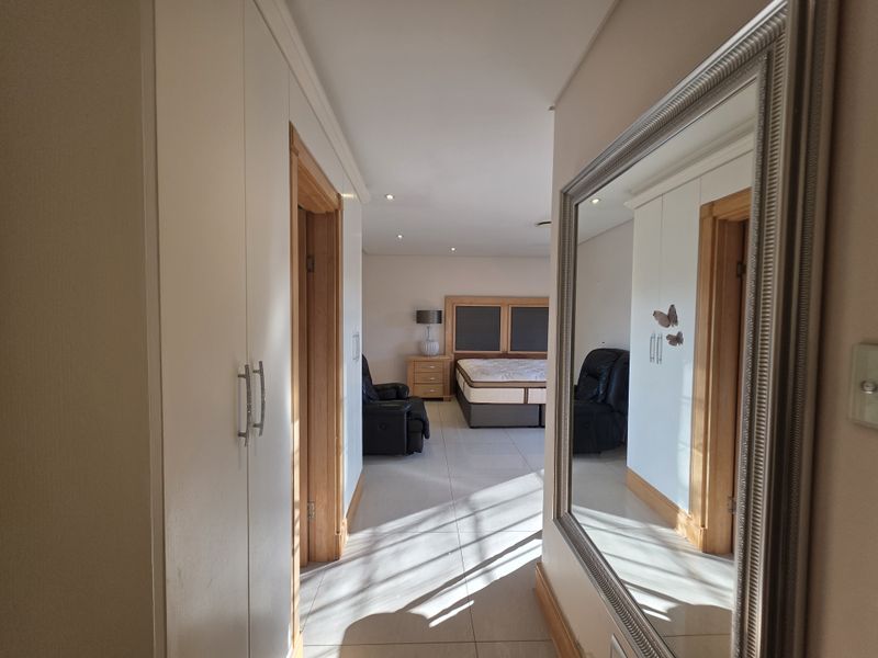 A spacious bedroom featuring built-in cupboards, tiled flooring, and recessed downlights, viewed from an adjacent hallway.