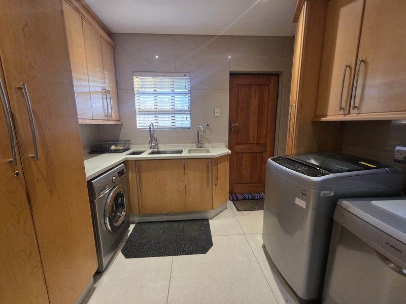 A functional laundry room featuring built-in timber cabinetry, double sink, tiled finishes, and direct access to an exterior door.