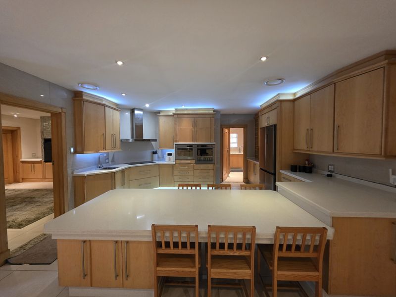 Spacious kitchen featuring light wood cabinetry, stone countertops, a large central island, and integrated appliances with modern recessed and cove lighting.