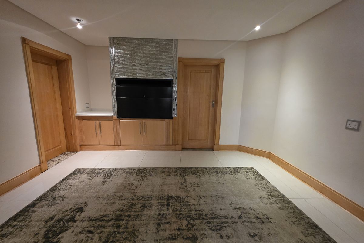 A spacious living area featuring a built-in fireplace with mosaic detailing, wooden door frames, and neutral tiled flooring.
