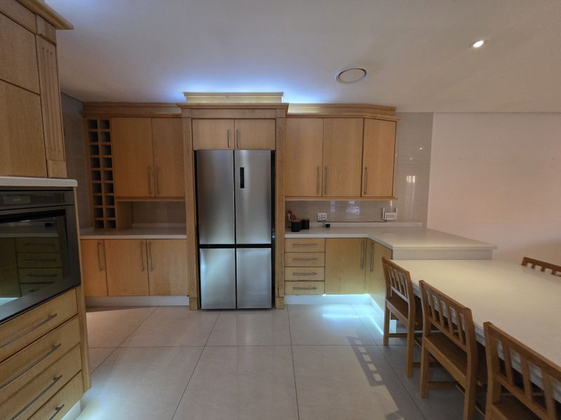 A well-appointed kitchen featuring light wood cabinetry, stone countertops, integrated appliances, and modern recessed lighting with a seamless tiled floor finish.