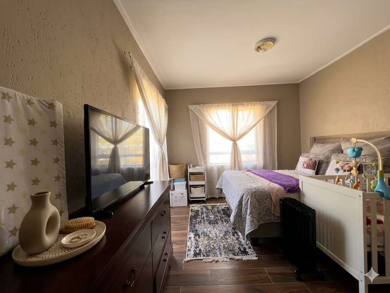 A well-maintained bedroom featuring tiled flooring, textured walls, and natural light through a window with curtains.