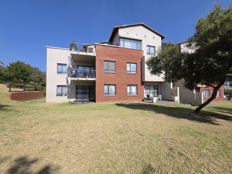 Rear view of a multi-story apartment building featuring a brick facade, private balconies with metal railings, and ground-floor patio access to a communal garden.