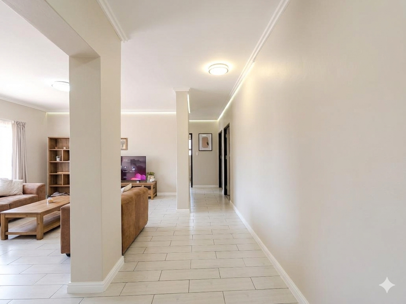 Bright open-plan living area featuring neutral tiled flooring, clean wall finishes, and modern recessed ceiling lighting with decorative cove molding.