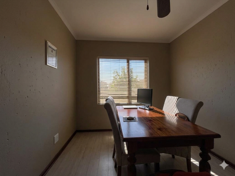 A functional home office space featuring laminate flooring, a central ceiling fan, and a window fitted with venetian blinds.