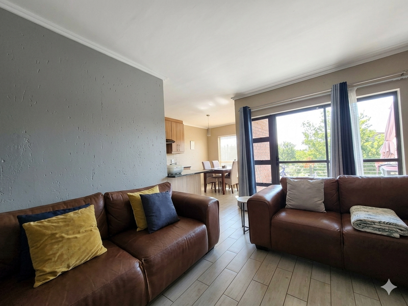 Open plan living and dining area featuring tiled floors, a sliding door to the balcony, and an adjoining kitchen with built-in cabinetry.