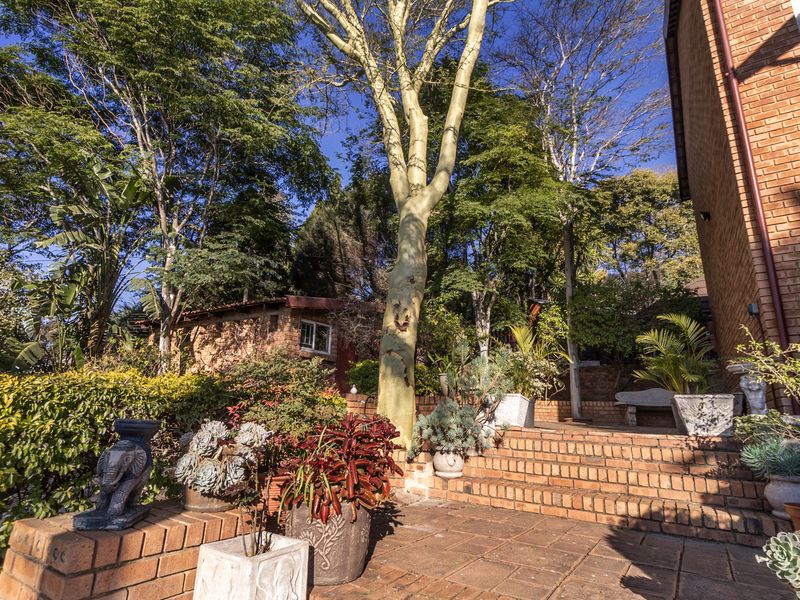 A landscaped rear garden area featuring brick paved stairs, retaining walls, and mature trees adjacent to the brick townhouse structure.