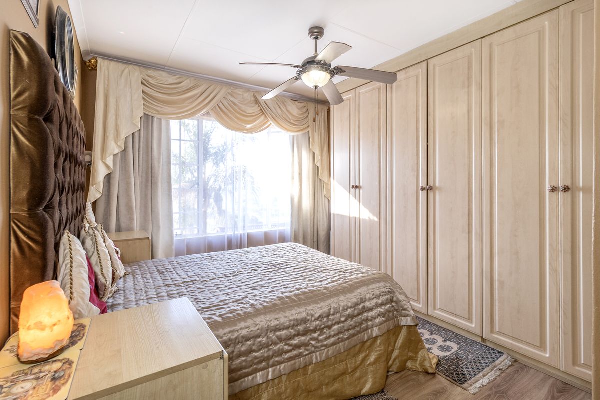 A well-maintained bedroom featuring extensive built-in cupboards, a ceiling fan, and laminate flooring, offering ample storage and comfortable living space.