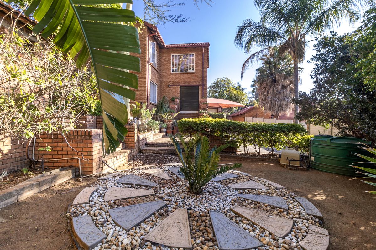A rear view of the townhouse featuring a brick facade, landscaped garden with a decorative paved circle, and a water storage tank.
