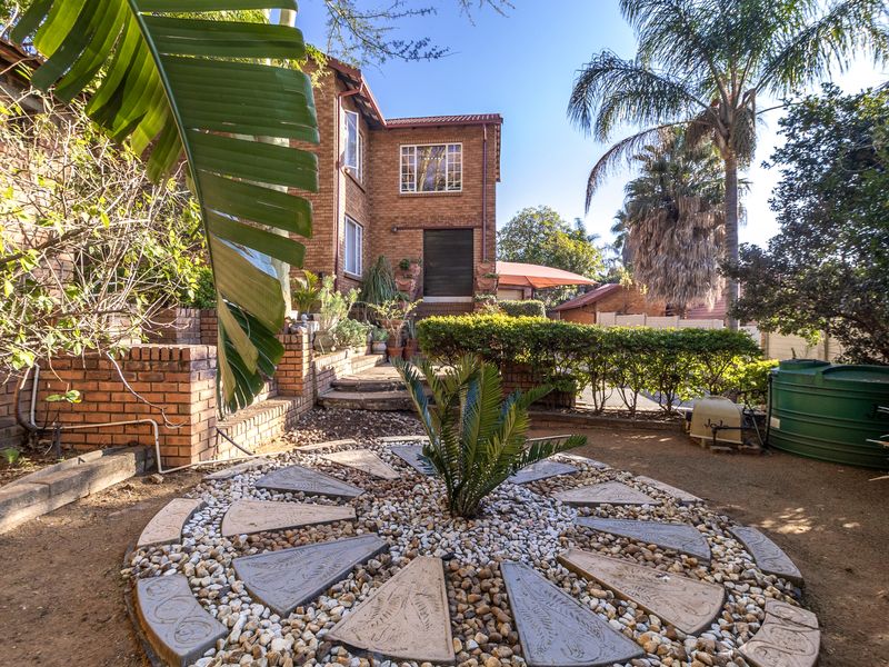 A rear view of the townhouse featuring a brick facade, landscaped garden with a decorative paved circle, and a water storage tank.