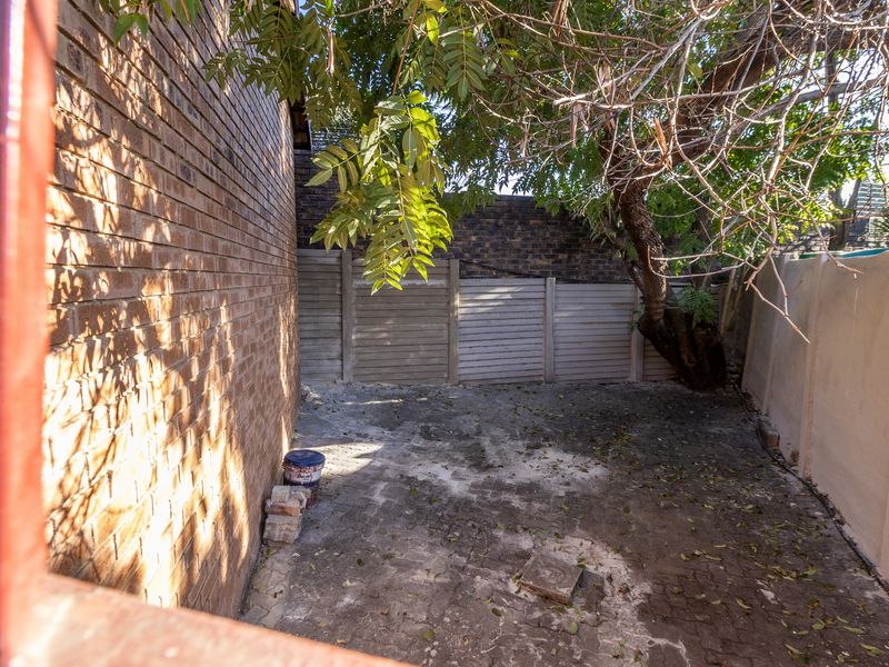 A private rear courtyard area featuring brick and concrete boundary walls with paved flooring and mature tree coverage.