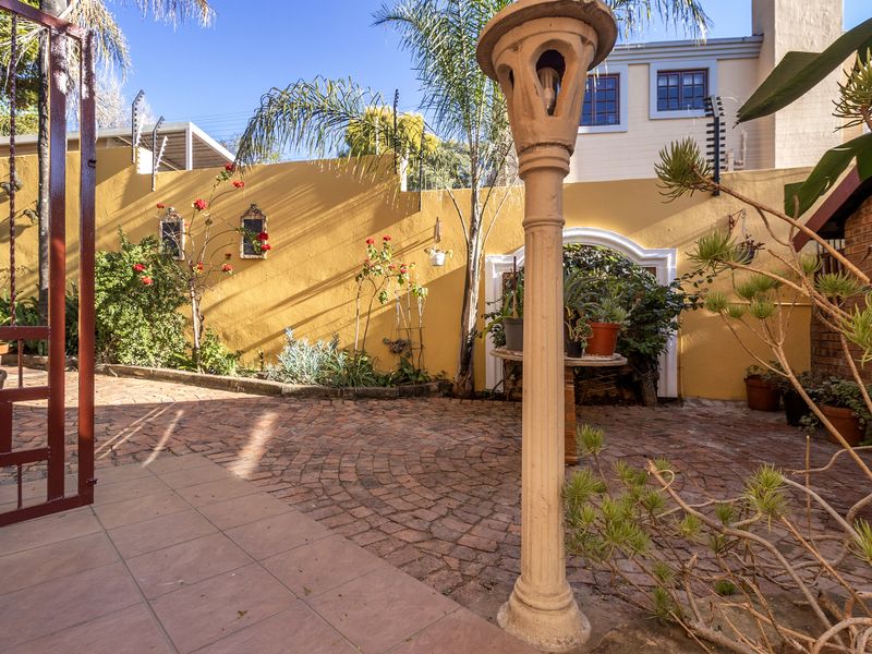 A private rear courtyard featuring brick paving, a decorative archway, and secure perimeter walling with electric fencing.