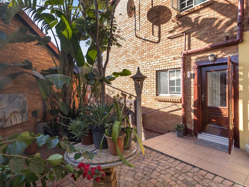 A rear exterior view of the townhouse featuring a brick facade, a tiled patio area, and established garden landscaping.