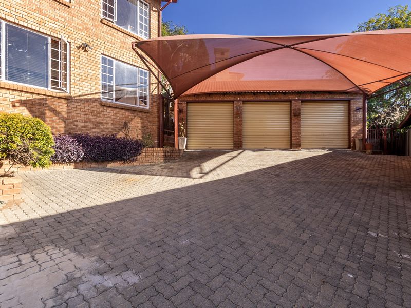 A well-maintained triple garage featuring roller shutter doors, a paved driveway, and a large shade sail structure.