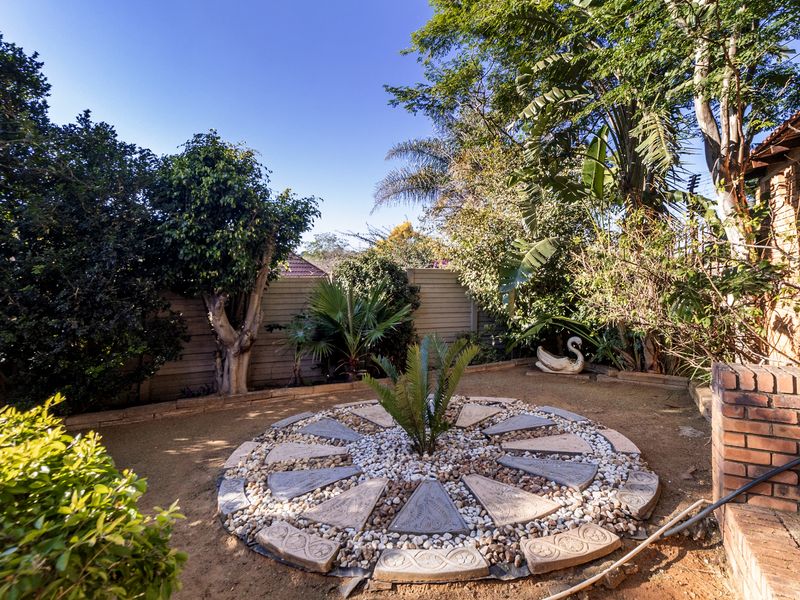 A private garden area featuring a decorative circular paved feature, established trees, and brick boundary walls.