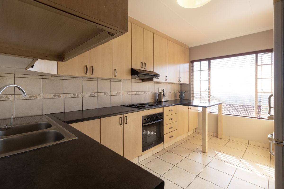 Functional kitchen featuring light wood cabinetry, dark countertops, built-in oven and hob, tiled backsplash, and ample natural light from the large window.