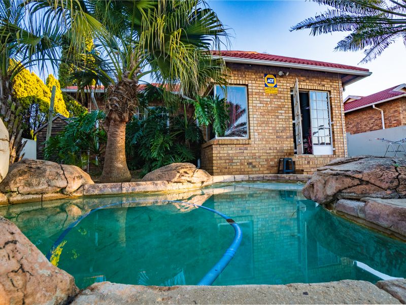 A backyard pool area featuring a rock-lined swimming pool set against a face brick townhouse exterior with a tiled roof.