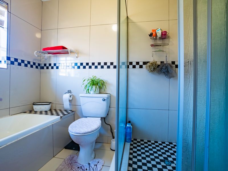 A functional bathroom featuring a bathtub, separate shower enclosure, and tiled finishes with a classic checkerboard accent border.