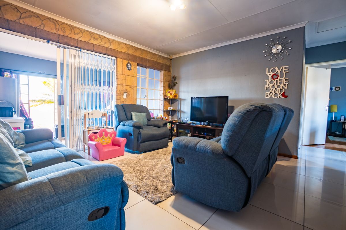 A comfortable living room featuring tiled flooring, a stone-cladding feature wall, and a security gate leading to the outdoor area.