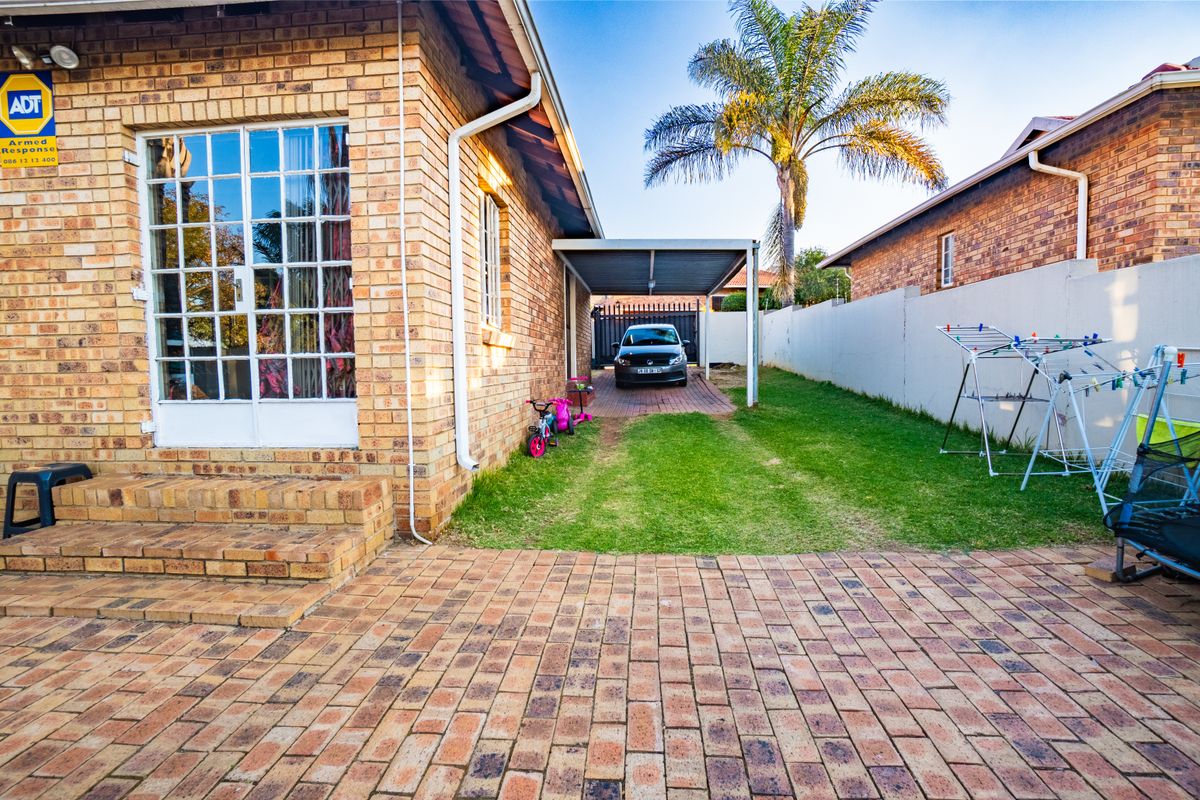 Rear exterior view of the townhouse featuring a paved patio area, a private carport, and a manageable garden space with boundary walling.
