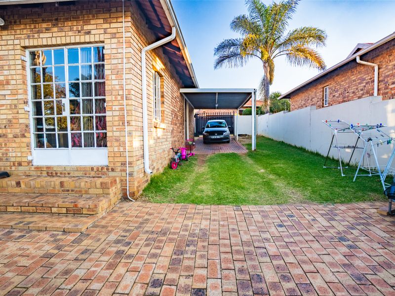 Rear exterior view of the townhouse featuring a paved patio area, a private carport, and a manageable garden space with boundary walling.