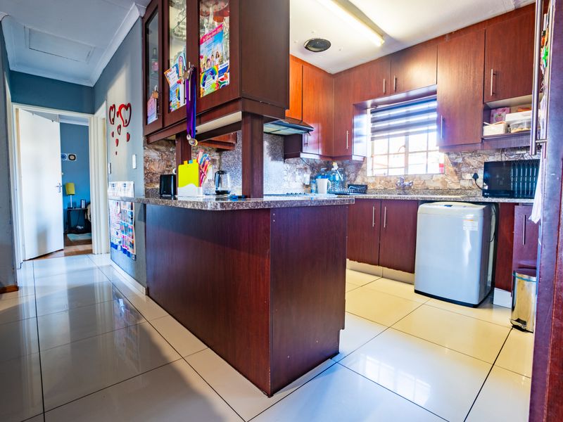 A functional kitchen featuring dark wood cabinetry, granite countertops, tiled flooring, and a breakfast bar, providing a practical layout for daily meal preparation.