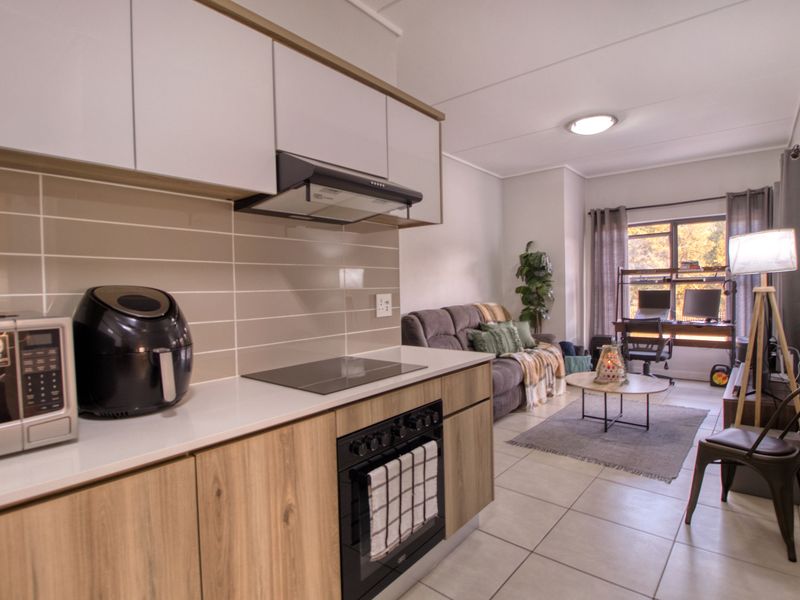 Modern open-plan living area featuring a contemporary kitchen with built-in cabinetry, electric hob, oven, and tiled flooring, seamlessly flowing into the lounge space.