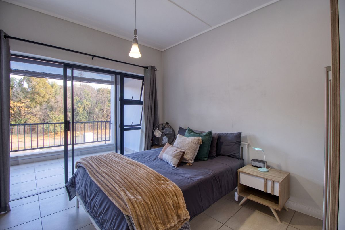 A well-lit bedroom featuring tiled flooring, a pendant light, and a large sliding glass door providing direct access to a private balcony.