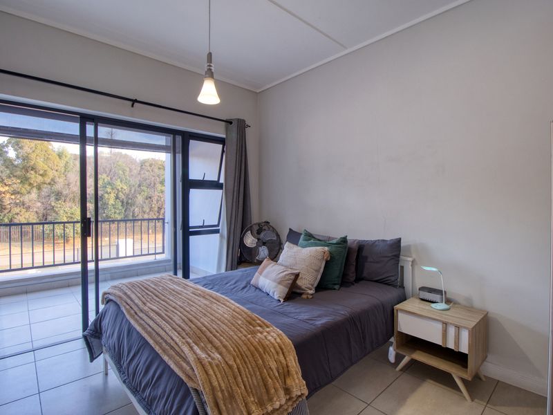 A well-lit bedroom featuring tiled flooring, a pendant light, and a large sliding glass door providing direct access to a private balcony.