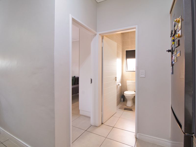 A clean, neutral hallway providing access to a bathroom and adjacent bedroom, featuring tiled flooring and standard internal door frames.