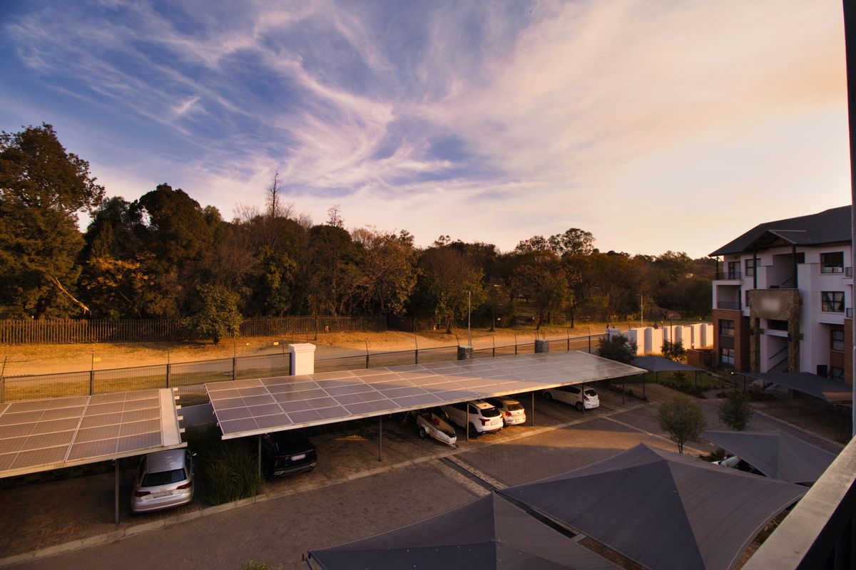 Elevated view of the apartment complex parking area featuring solar panel carports, paved driveway, and shade sail structures.