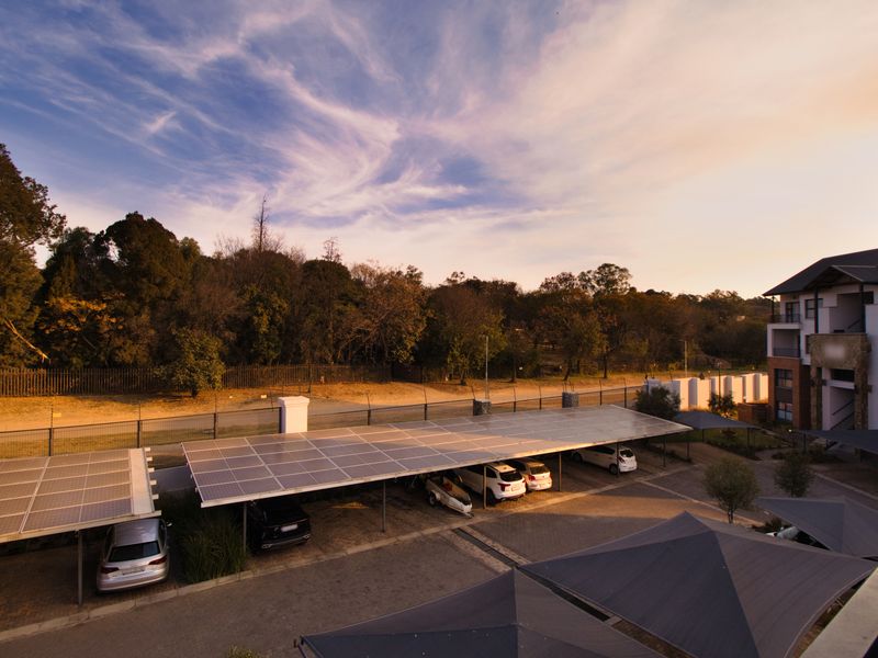 Elevated view of the apartment complex parking area featuring solar panel carports, paved driveway, and shade sail structures.