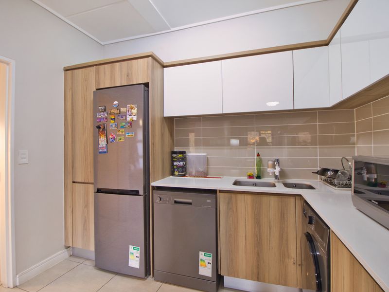 Modern kitchen featuring wood-grain cabinetry, white upper cabinets, subway tile backsplash, and integrated appliance spaces with durable tiled flooring.