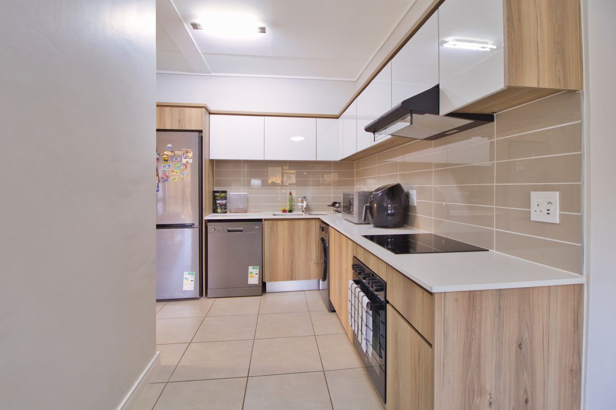 Modern kitchen featuring wood-grain cabinetry, white upper cabinets, sleek countertops, ceramic tile backsplash, and integrated appliances including an oven and cooktop.