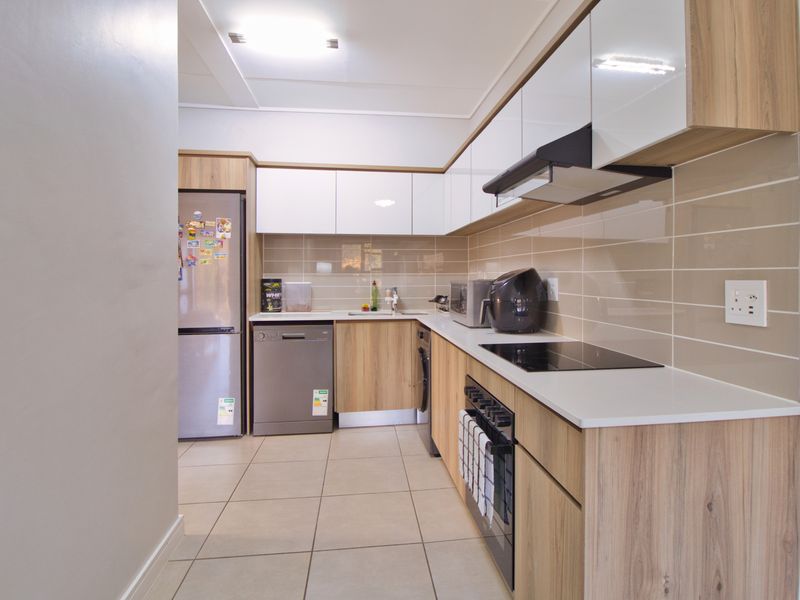 Modern kitchen featuring wood-grain cabinetry, white upper cabinets, sleek countertops, ceramic tile backsplash, and integrated appliances including an oven and cooktop.