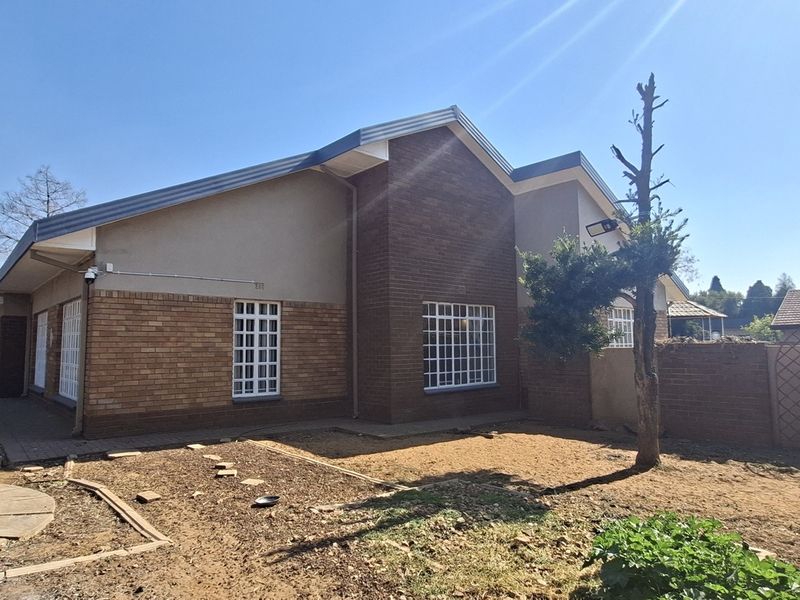 Rear view of the house featuring a brick facade, tiled roof, security bars on windows, and a paved walkway leading to the garden area.