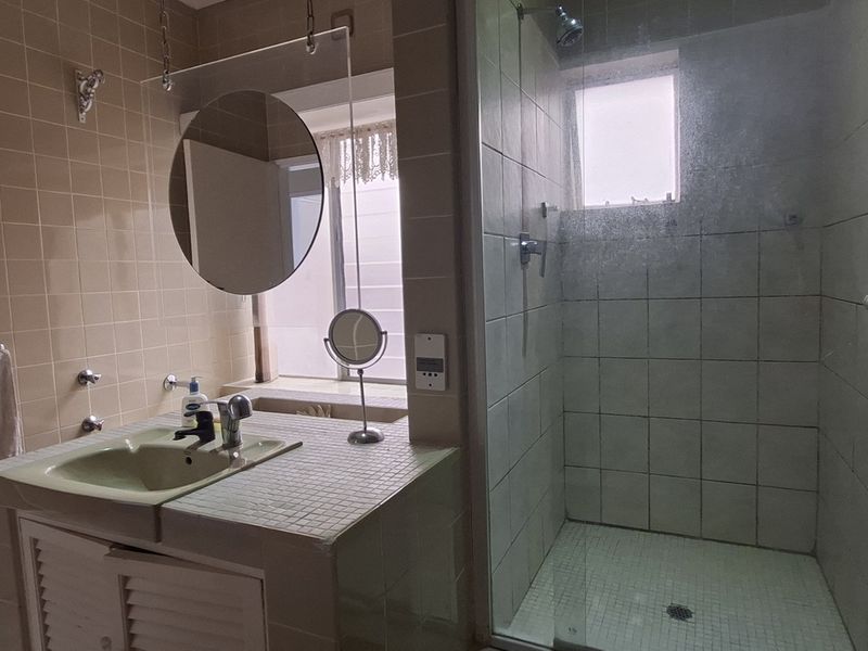 A functional bathroom featuring a tiled shower enclosure and a built-in vanity with a ceramic basin, showcasing a classic, dated aesthetic.