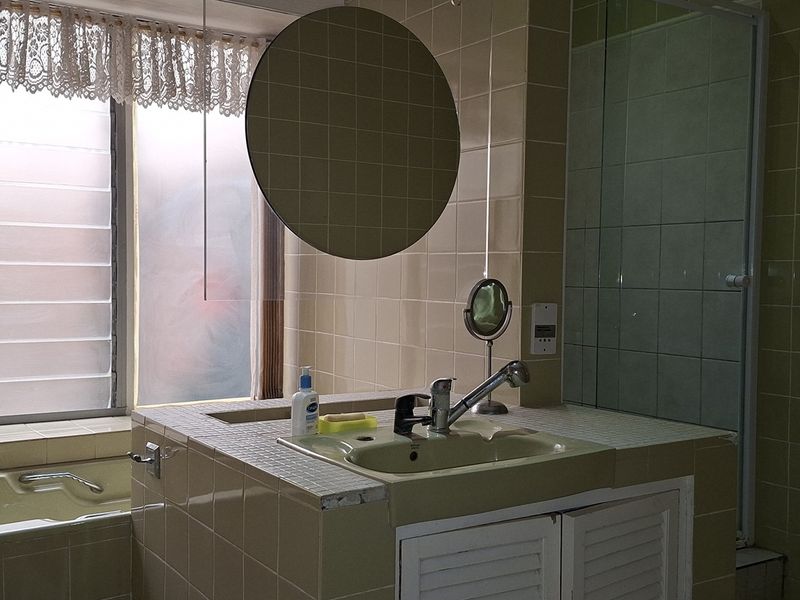 A dated bathroom featuring a built-in vanity, tiled bathtub, and separate shower enclosure with louver windows.