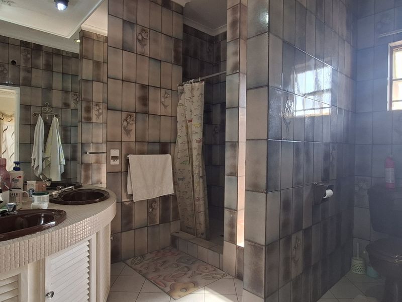 A dated bathroom featuring a dual vanity, tiled walls, a shower enclosure, and a toilet, offering potential for a modern renovation.