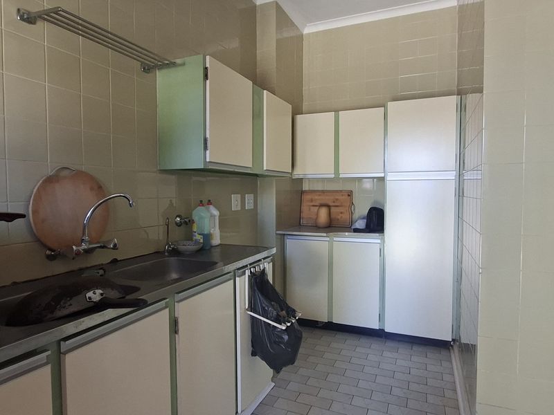 A functional scullery area featuring built-in cabinetry, tiled walls, and a stainless steel sink, offering a practical space for food preparation and cleanup.
