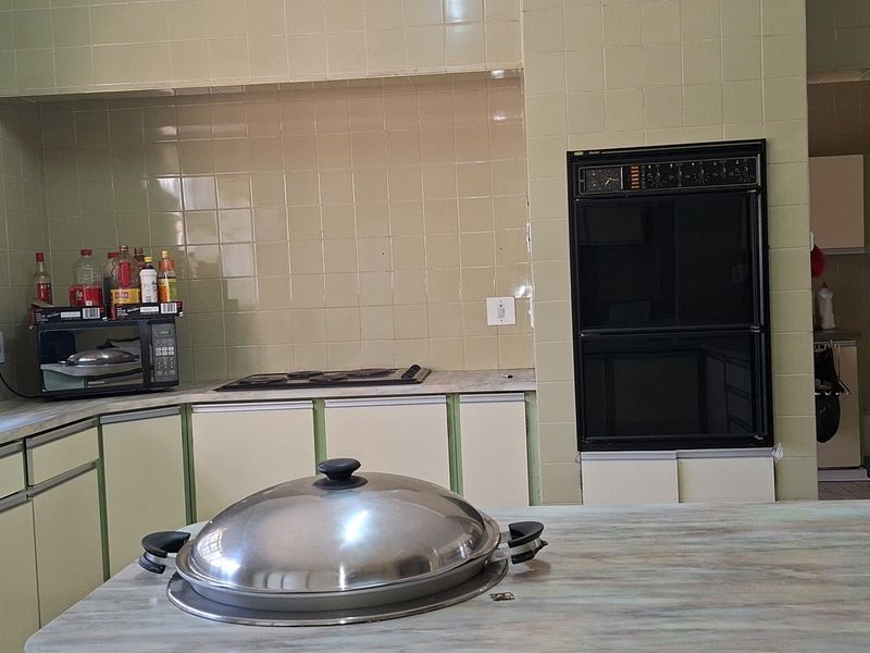 A dated kitchen featuring original tiled walls, built-in oven, electric hob, and laminate countertops, offering significant potential for a modern renovation.
