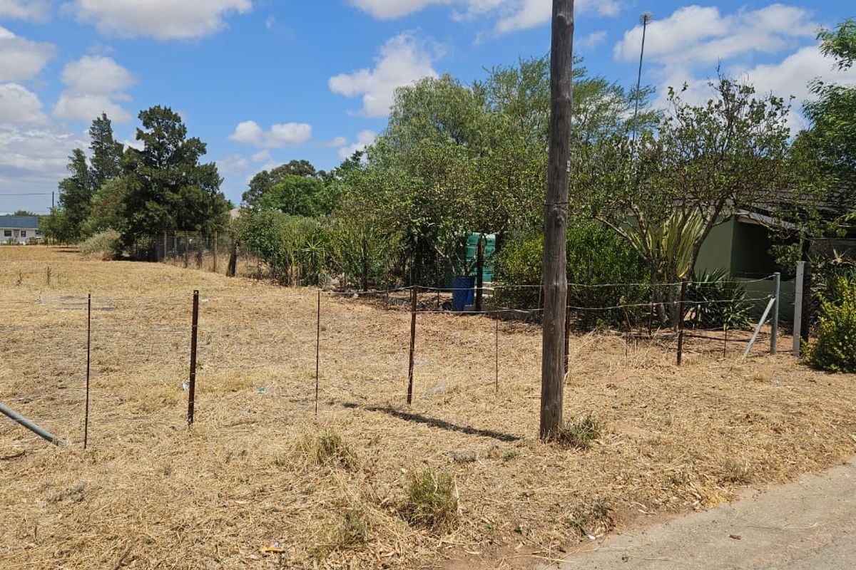 A vacant residential plot featuring wire fencing, mature trees, and a utility pole, offering a clear view of the undeveloped land.