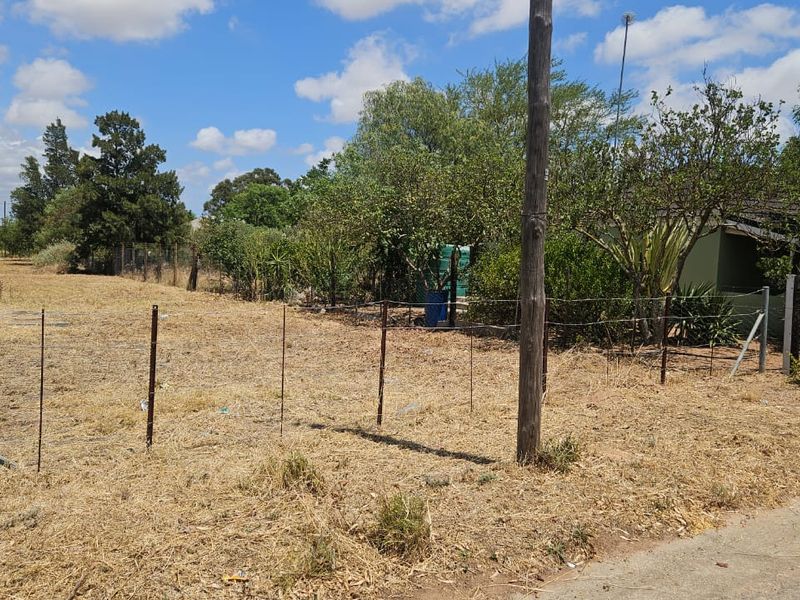 A vacant residential plot featuring wire fencing, mature trees, and a utility pole, offering a clear view of the undeveloped land.