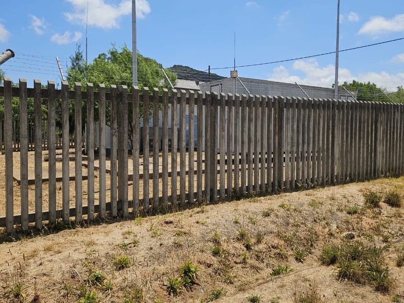 A view of the property boundary featuring concrete palisade fencing with security barbed wire and a utility structure visible in the background.