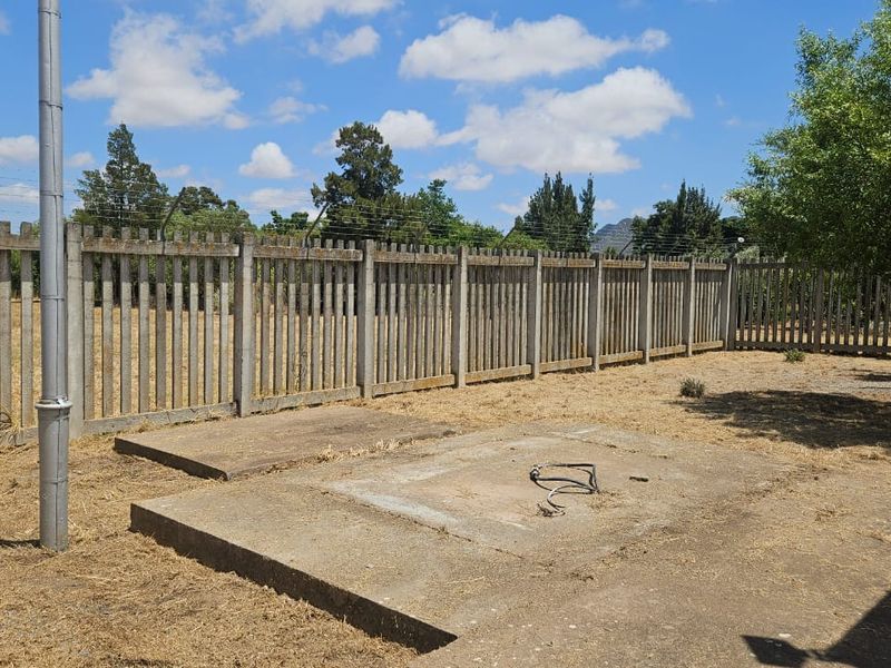A vacant residential plot featuring concrete palisade fencing with barbed wire, a concrete slab foundation, and a utility pole on the property.